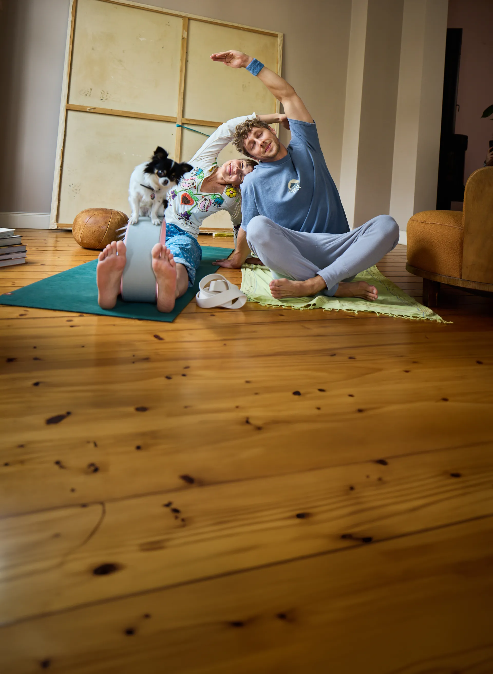 Zwei Menschen in einer Yoga-Pose mit einem kleinen Hund daneben